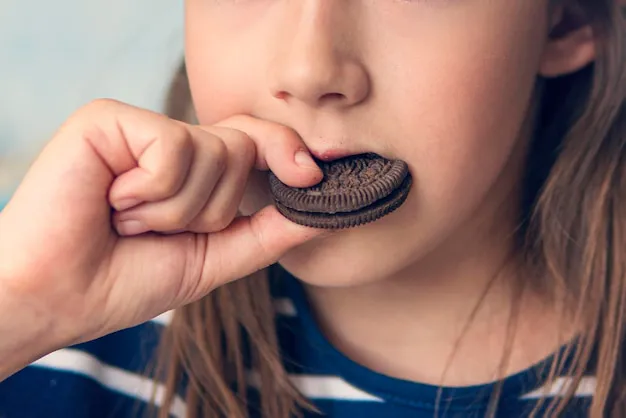 cerca-chica-comiendo-galleta-chocolate-redonda-sentada-cocina-casa-comida-danina-pero-deliciosa-dulzura_431724-4512